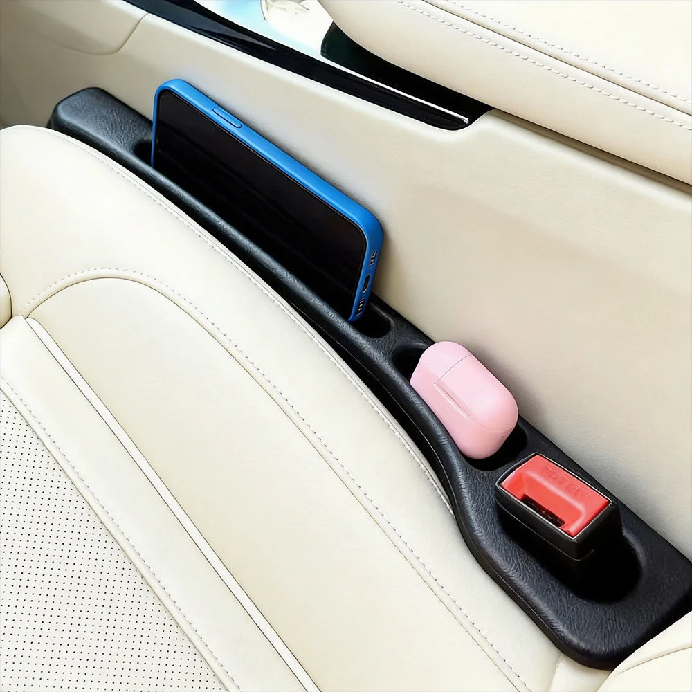 A blue smartphone and a pink accessory are placed in the gap between a car seat and a vehicle interior panel.