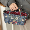 A hand holds a quilted fabric storage basket with a blue floral pattern, featuring a red lining, against a light background.