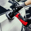 A hand wearing a glove is using a red and black car polishing tool on a white car surface.