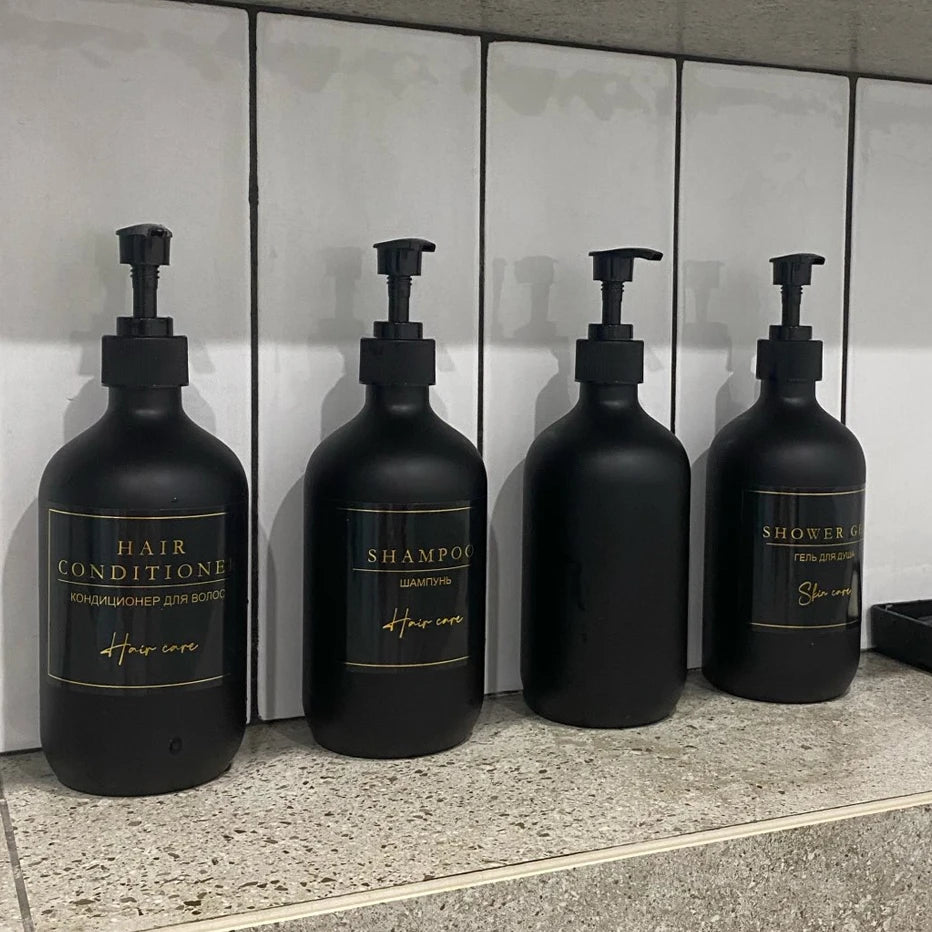 Three black refillable bottles of hair products including conditioner, shampoo, and shower gel displayed on a counter.
