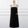 Black canvas kitchen apron with leather straps and large pockets displayed on a mannequin.