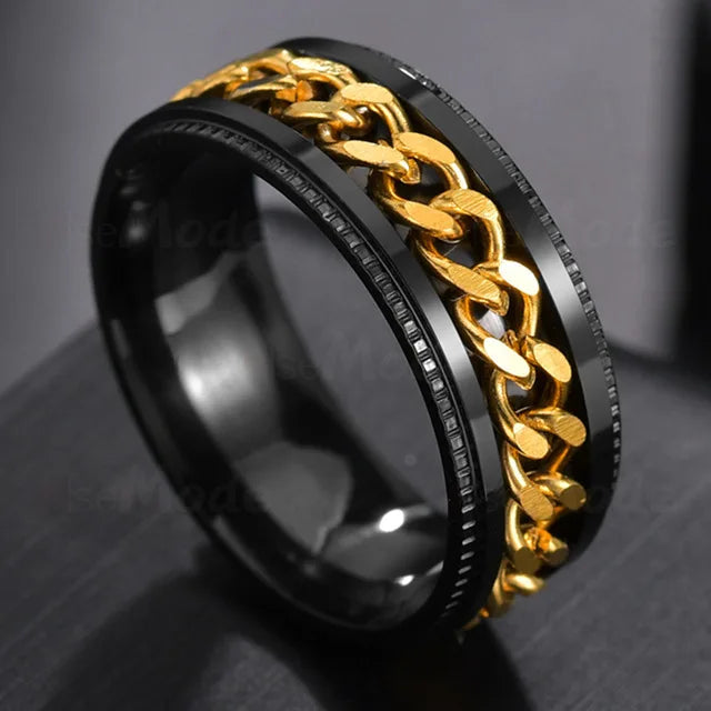 A close-up shot of a black stainless steel spinner ring with a gold chain detail.