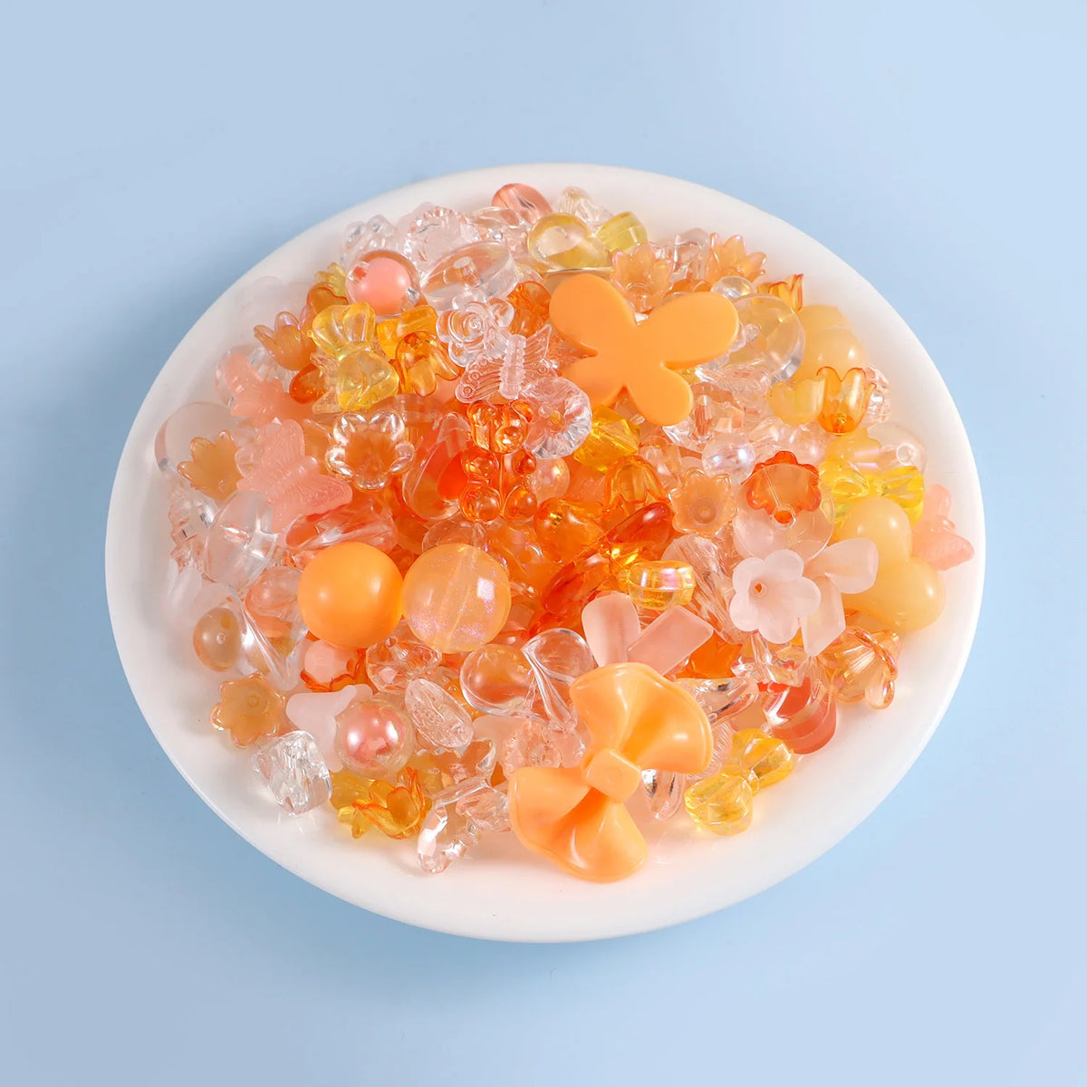 A pile of colorful acrylic beads in shades of orange, pink, and yellow on a white plate.