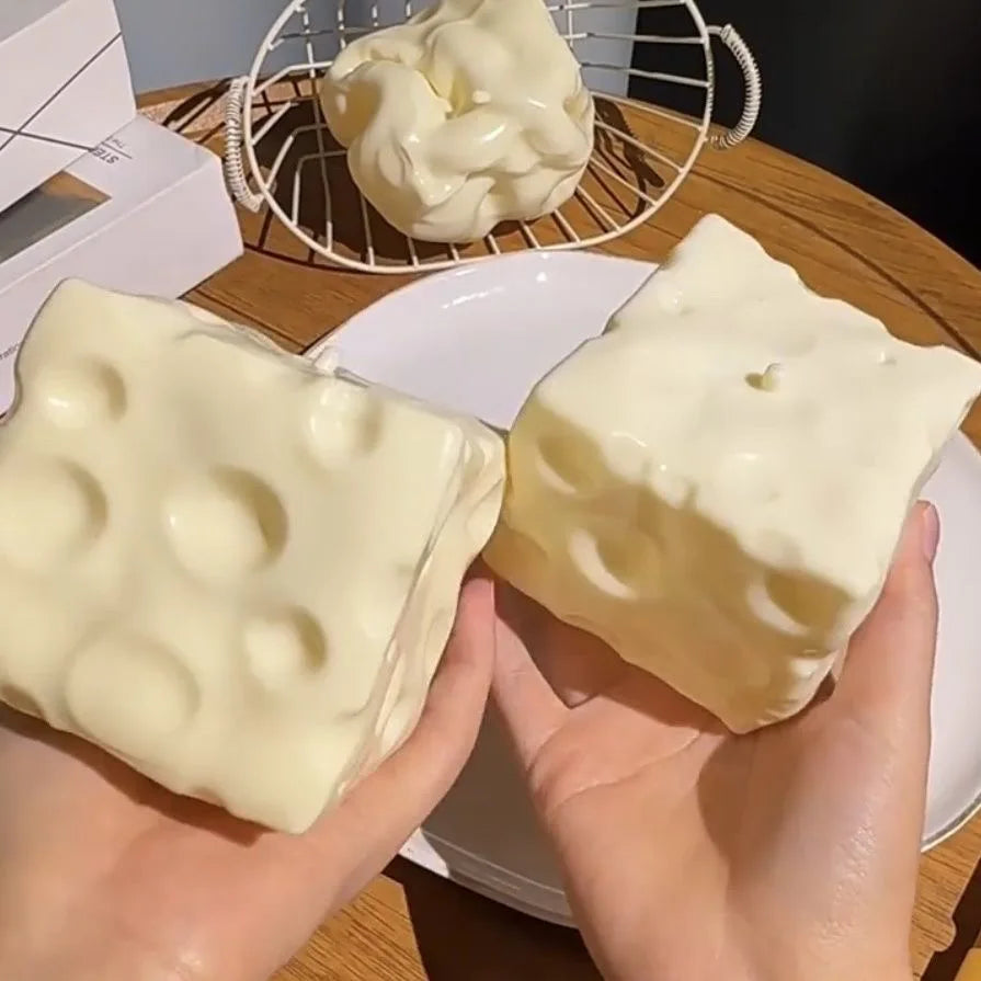Two blocks of realistic cheese squishy stress relief fidget toys are displayed on a white plate.