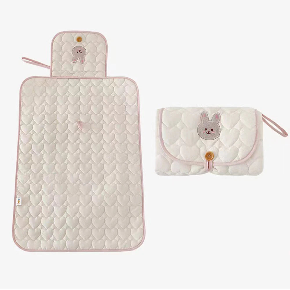A light pink quilted foldable portable diaper changing pad with a rabbit design.