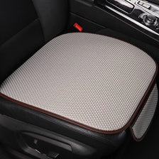 A beige breathable ice silk car seat cushion with a brown trim is shown in a black car interior.