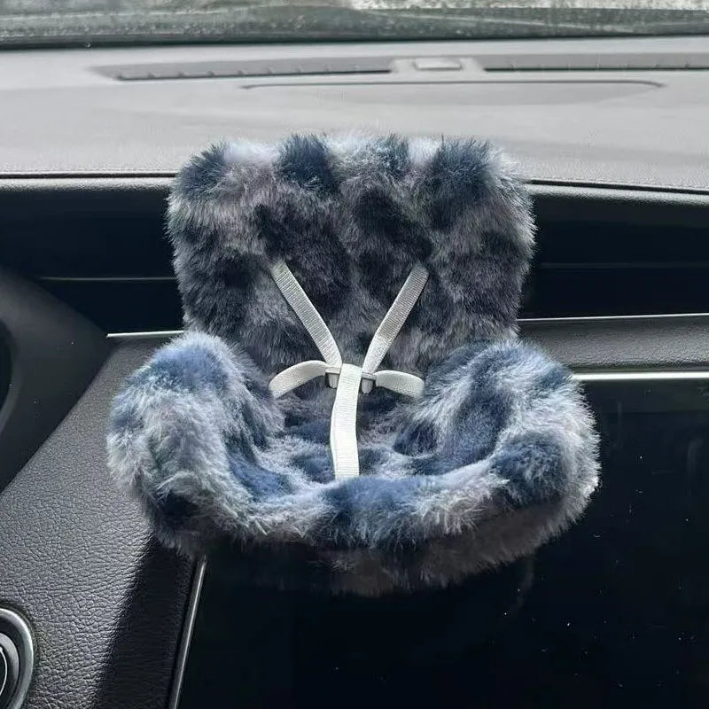 A fluffy blue faux fur vent decoration shaped like a miniature doll seat car is shown inside a car interior.