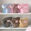 Three cosmetic bags in various shades of pink and blue leopard print with fuzzy handles displayed on a white shelf.