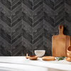 A wooden cutting board and bowls are displayed on a white surface against a dark gray herringbone patterned wall.