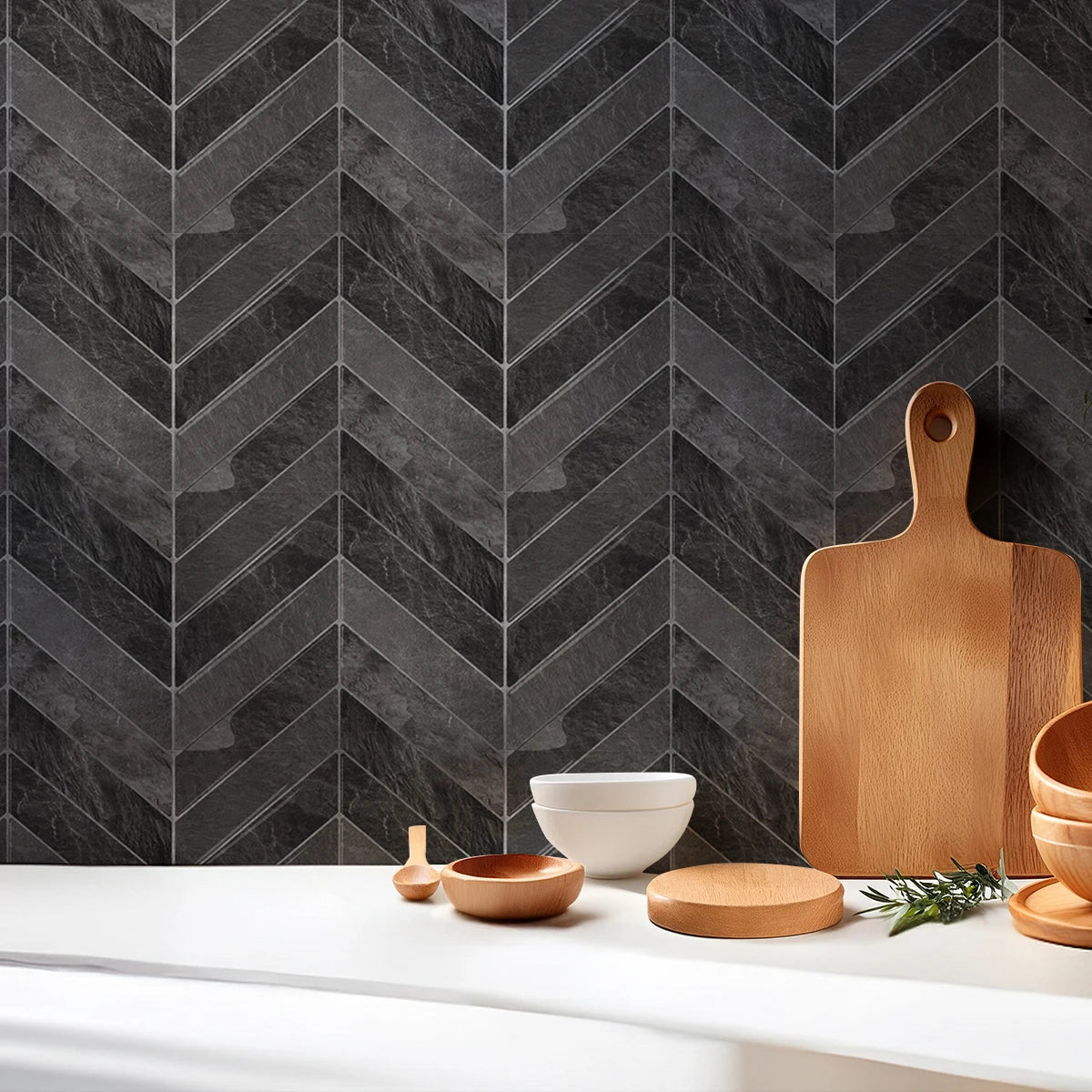 A wooden cutting board and bowls are displayed on a white surface against a dark gray herringbone patterned wall.