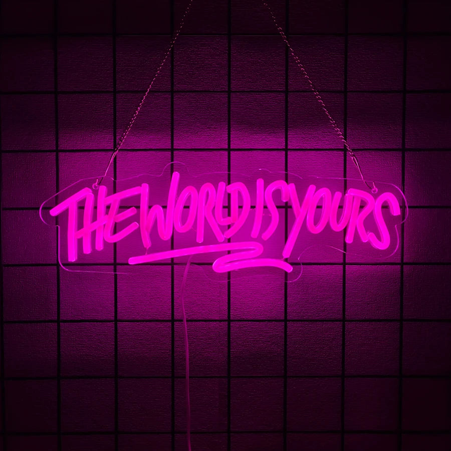 A neon sign spelling out THE WORLD IS YOURS in bright pink against a dark purple grid background.