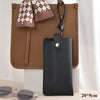 A black leather glasses case with a checkered fabric flap is displayed on a brown leather bag.