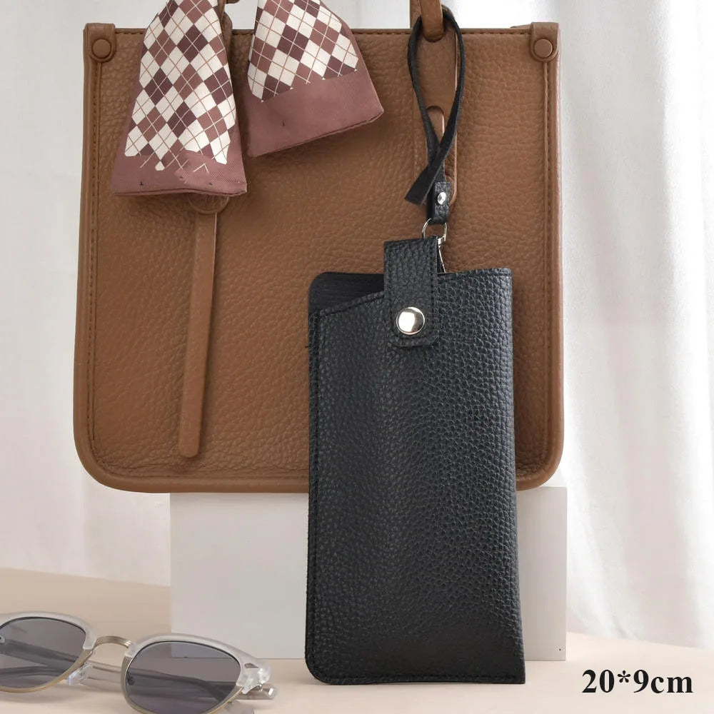 A black leather glasses case with a checkered fabric flap is displayed on a brown leather bag.