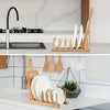 A wooden bamboo dish drying rack holding white plates and cutlery on a kitchen counter.