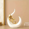A white ceramic sculpture shaped like a stylized leaf or crescent, with a gold metallic accent, displayed on a light surface.