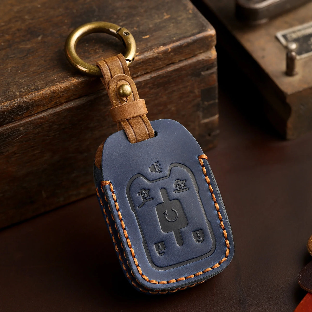 A dark blue leather key fob case with a brass ring attached, resting on a wooden box.