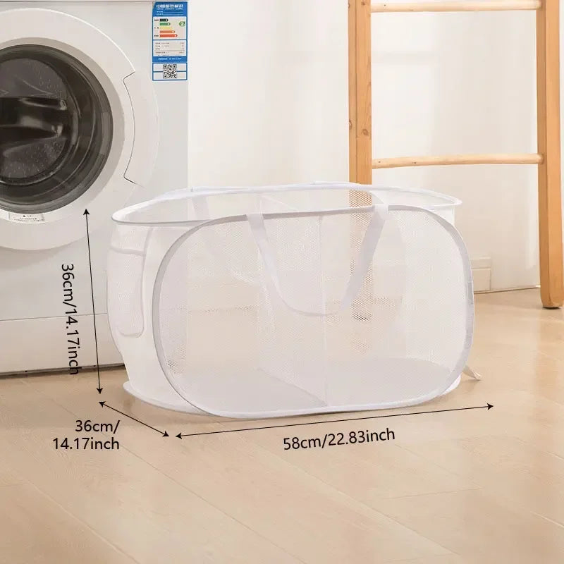 A white folding mesh laundry basket with handles is shown on a wooden floor next to a washing machine.