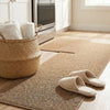 A woven jute kitchen runner rug with light beige slippers and white towels on a wooden floor.