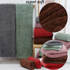 A stack of super soft bath towels in various shades of green, brown, and coral velvet.