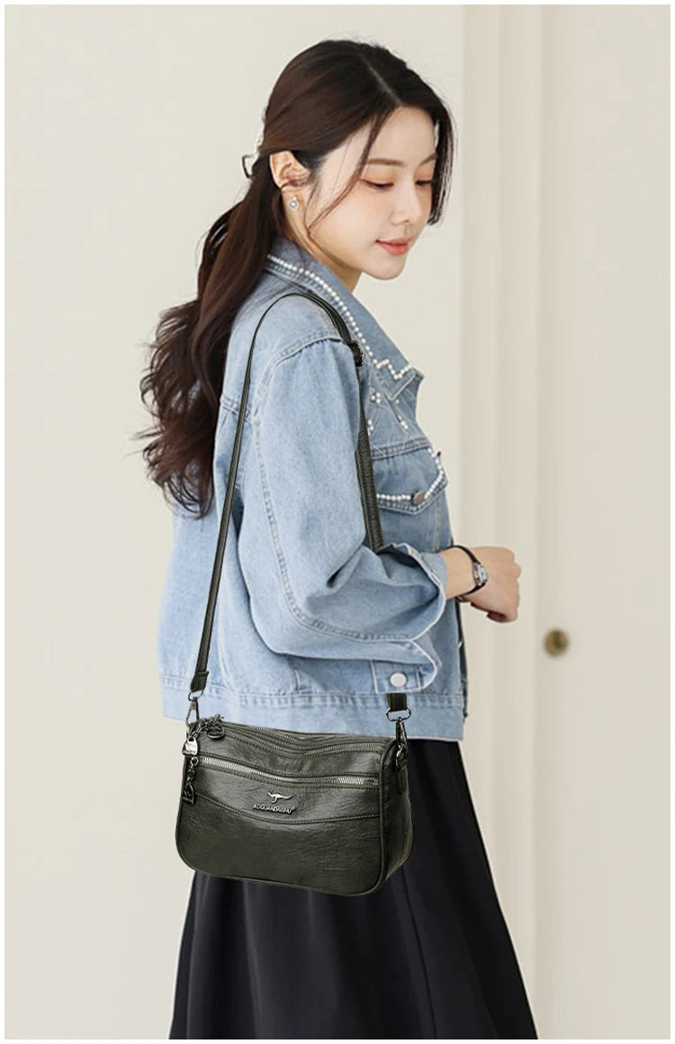 A woman models a dark green compact square crossbody bag with silver hardware and a denim jacket.
