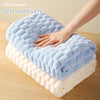 A hand is gently touching a fluffy blue cloud velvet bath towel layered on a white plush towel.