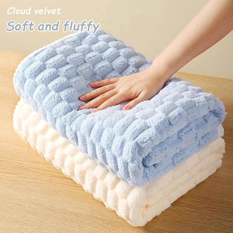A hand is gently touching a fluffy blue cloud velvet bath towel layered on a white plush towel.