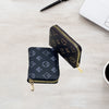 A black zippered card holder wallet with gold accents is placed on a light wooden surface next to a laptop and pen.
