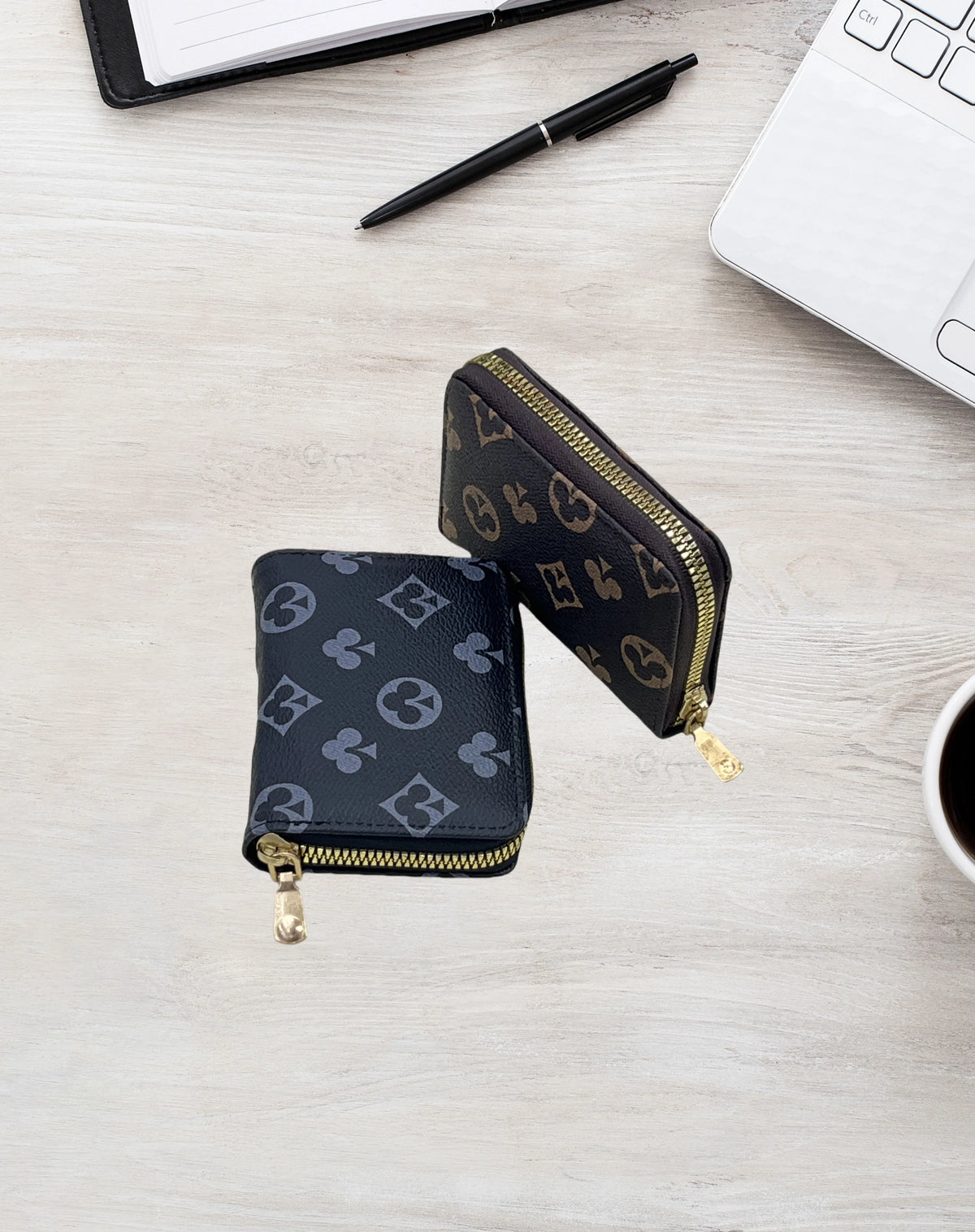 A black zippered card holder wallet with gold accents is placed on a light wooden surface next to a laptop and pen.