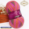 A skein of gradient dyed wool blend yarn in shades of pink, purple, and orange is displayed next to a wooden box.