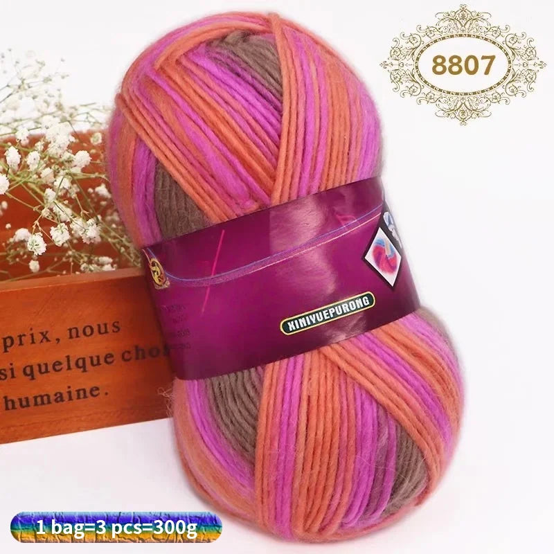 A skein of gradient dyed wool blend yarn in shades of pink, purple, and orange is displayed next to a wooden box.