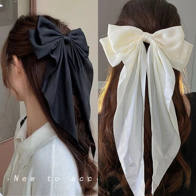 A close-up of a dark gray silk bow hair clip tied in a large bow on a woman's dark hair.