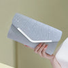 A light gray pleated glitter envelope clutch with a white strap is held by a hand.