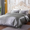 A luxurious silver silky duvet cover set displayed on a bed with a white upholstered headboard and modern decor.