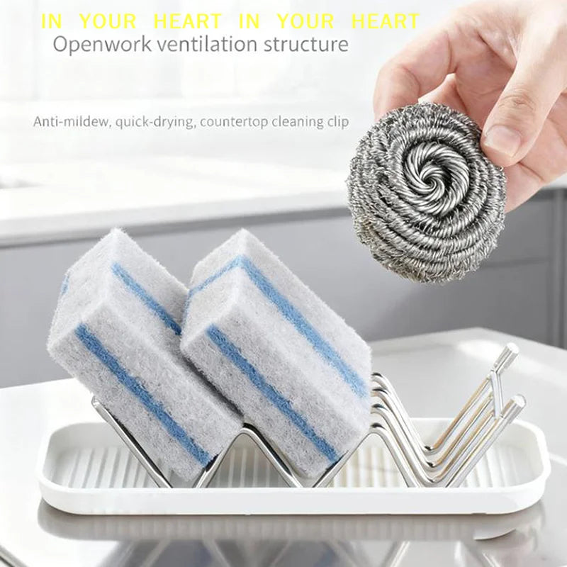A hand holds a coiled gray cleaning sponge, next to two blue and white cleaning sponges resting in a stainless steel holder o