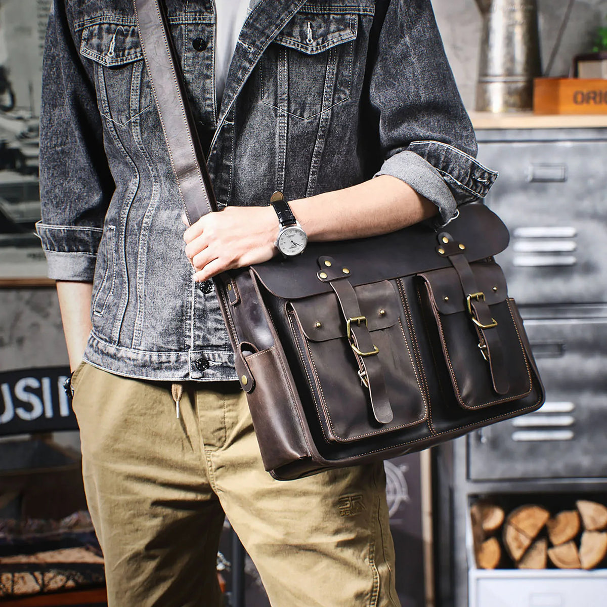 Eine Person hält eine braune Vintage-Ledertasche für Laptops, gepflegt mit einer grauen Jeansjacke und Khakihosen.