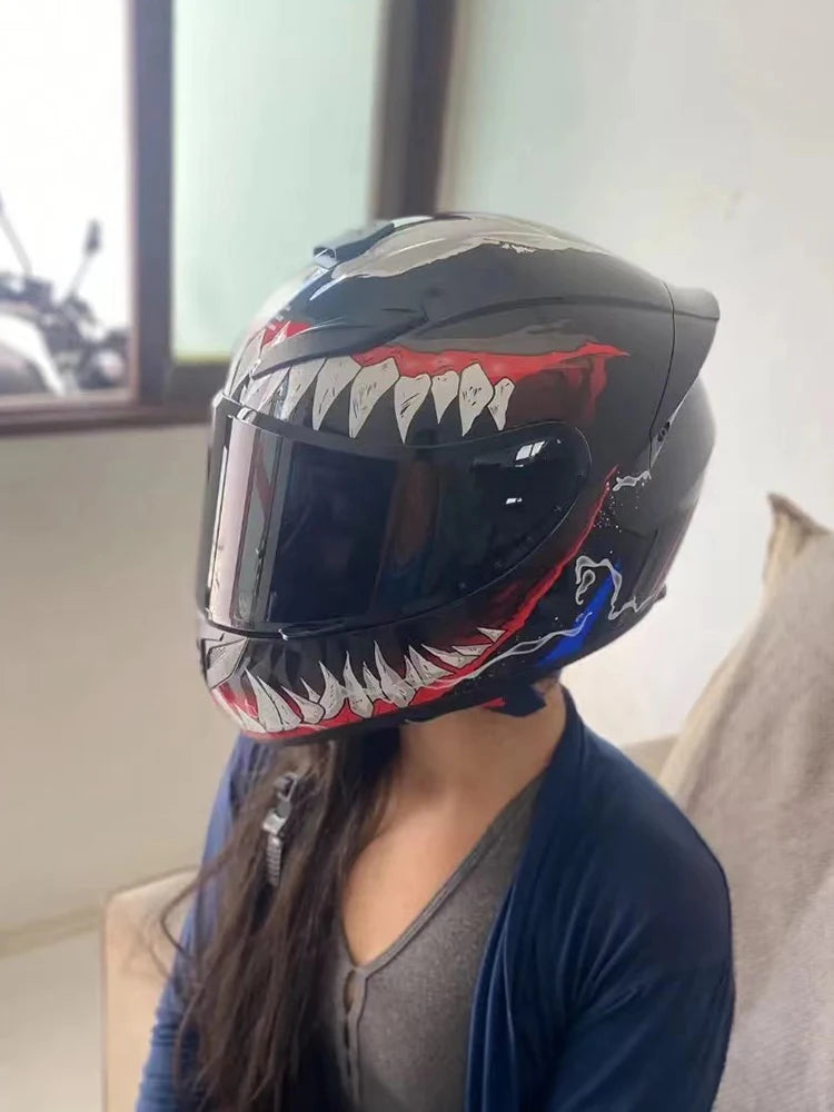 A black full-face motorcycle helmet with a fierce, toothy graphic design is displayed indoors.