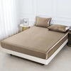 Beige Satin-Bettwäsche-Set mit zwei passenden Kissenbezügen auf einem weißen Bettrahmen in einem hellen Raum.