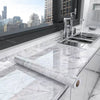 A stainless steel kitchen sink and faucet installed in a white marble countertop with a rolled marble effect film.