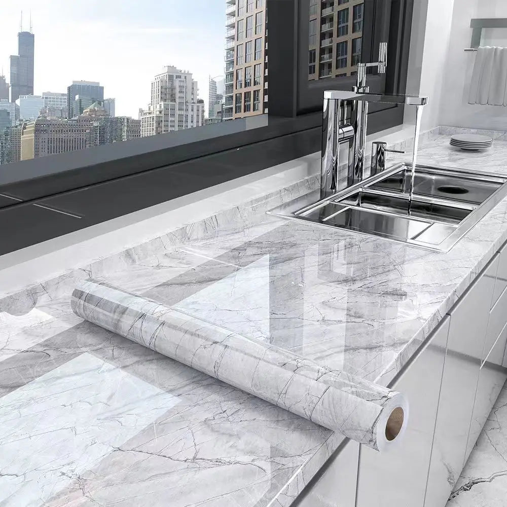 A stainless steel kitchen sink and faucet installed in a white marble countertop with a rolled marble effect film.