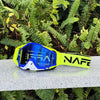 A pair of blue and yellow NAFE motocross goggles resting on a gray surface amidst green foliage.