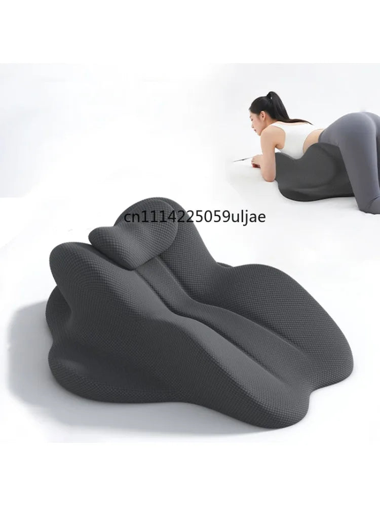 A dark gray ergonomic memory foam reading pillow is shown lying on a white surface.