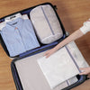 A hand is placing a white mesh laundry bag into a dark storage box alongside other similar bags.