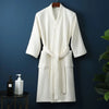 A white lightweight cotton waffle robe hanging on a dark blue wall.