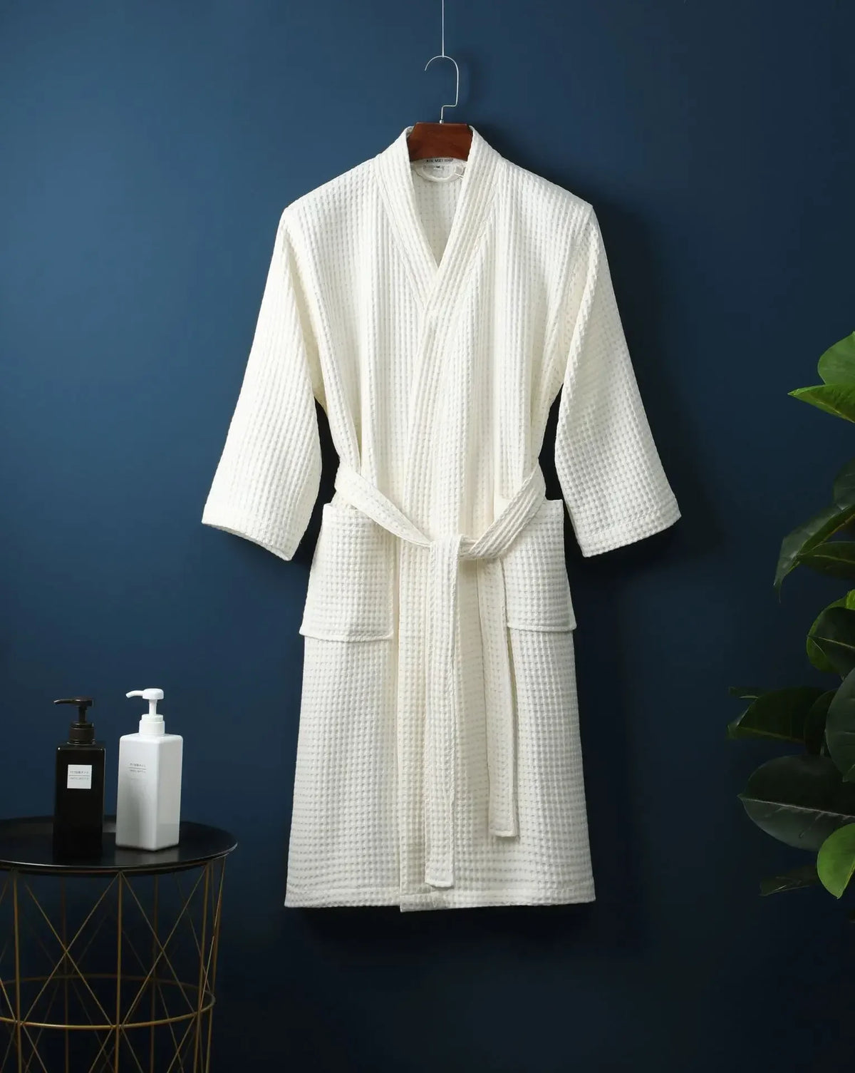 A white lightweight cotton waffle robe hanging on a dark blue wall.