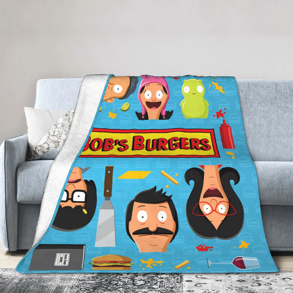 A colorful cartoon-themed throw blanket featuring characters from Bob's Burgers on a gray sofa.