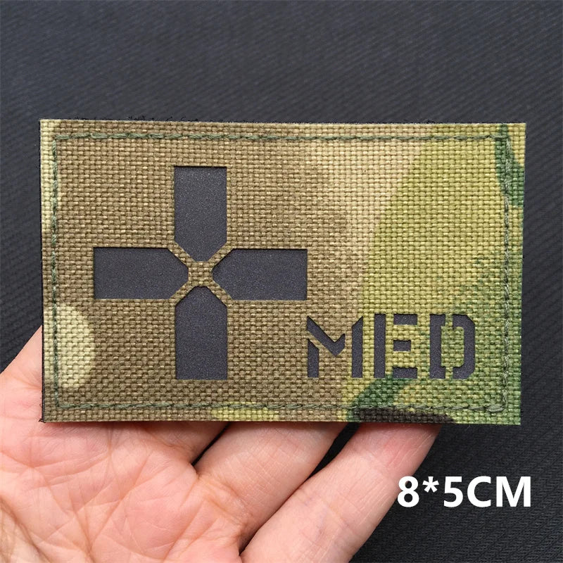 A rectangular olive green tactical patch featuring a black medical cross symbol and the letters MED on a hand.