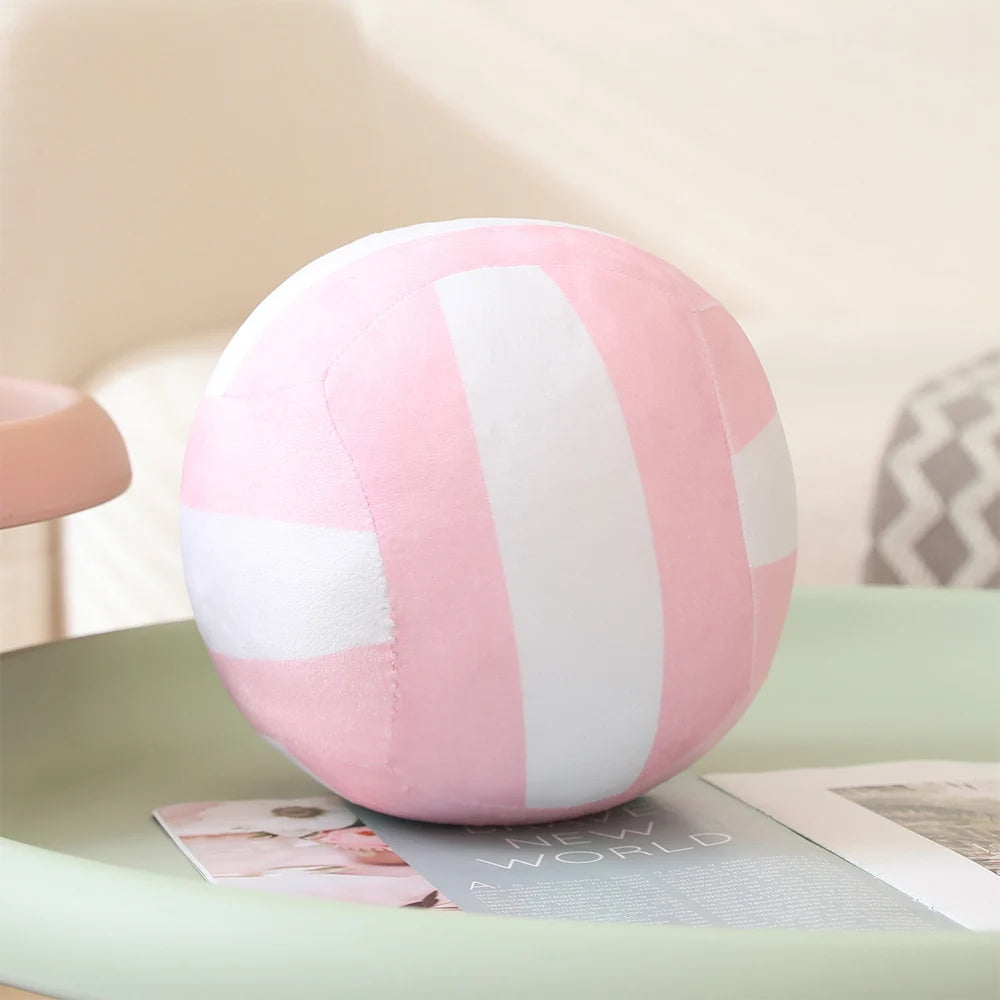 A pink and white striped simulation volleyball plush toy resting on a light green surface.