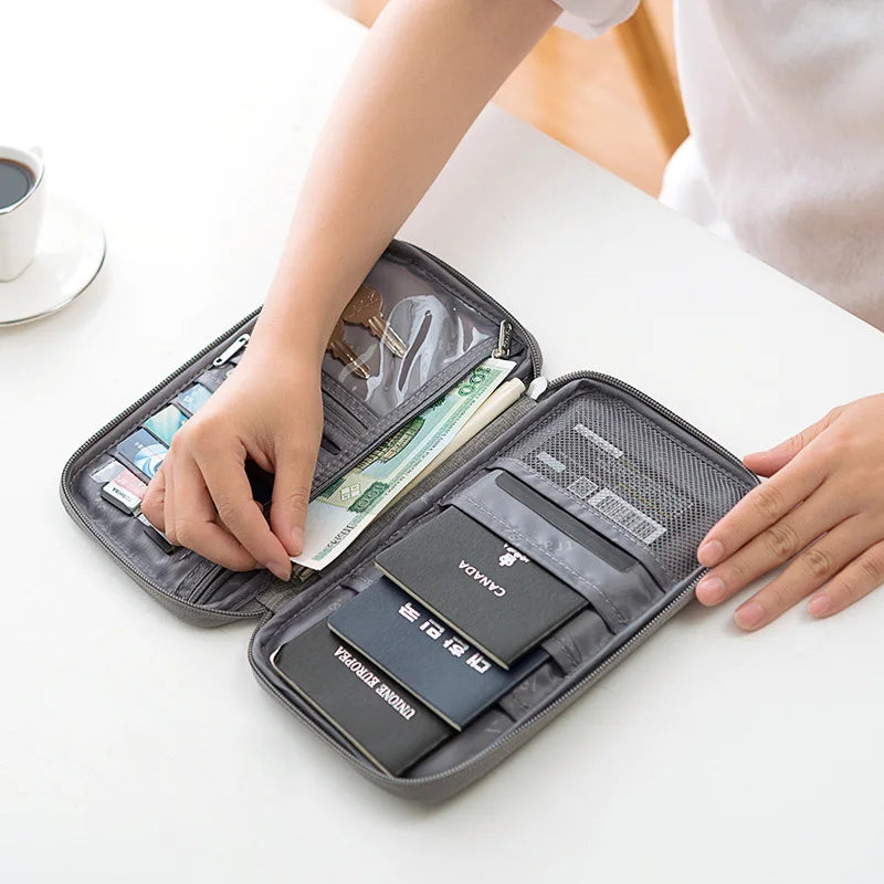 A hand is opening a dark gray waterproof passport and document organizer wallet showing various travel documents.