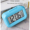 A light blue compact LED digital alarm clock with a clear screen resting on a piece of paper.