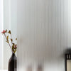 A dark vase with pink flowers sits in front of a white wall with vertical frosted stripe privacy film.